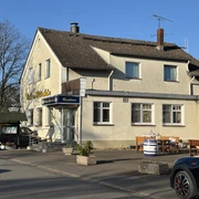 Zweistöckiges Gasthaus mit gelber Fassade, Sitzbänken vor dem Eingang, umgeben von Bäumen.