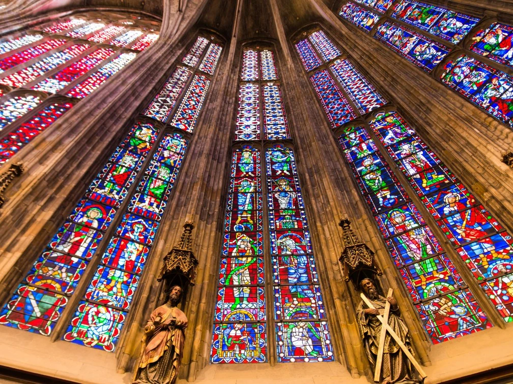 Aachener Dom Blick nach oben entlang der bunten Fenster des Aachener Doms, zwischen denen Säulen mit Statuen stehen.