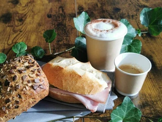 Kaffee und Sandwiches im Rüfenacht Bistro Zwei Becher Kaffee, ein Sandwich und ein Körnerbrötchen, arrangiert auf einem HolztischTwo mugs of coffee, a sandwich and a granola roll, arranged on a wooden tableDeux gobelets de café, un sandwich et un petit pain aux graines, disposés sur une table en bois