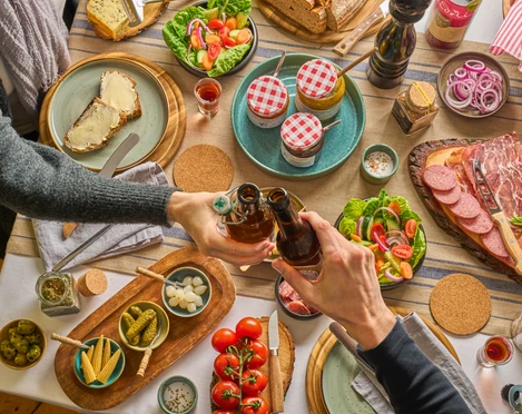 Gedeckter Tisch mit TYPISCH-neanderland Produkten und Ratuga Bier Einladender Tisch mit regionalen Produkten, Salaten und Ratuga Bier, Hände beim Anstoßen.