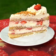 Torte Bauerncafé Oltmanns.jpg Tortenstück mit frischen Erdbeeren und Sahnehäubchen auf rustikal-rotem Tischdeckenmuster serviert.