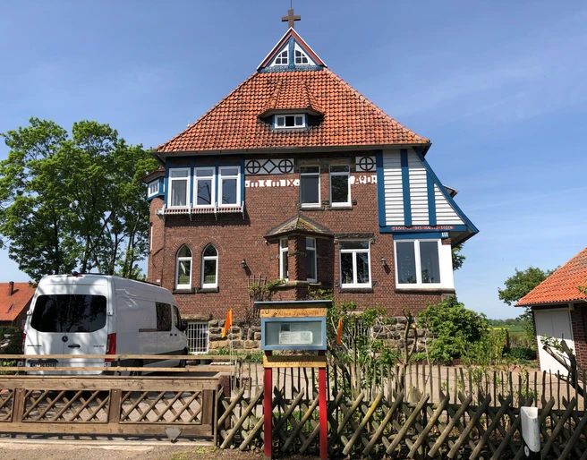 Pilgerherberge Altes Pfarrhaus Historisches rotes Backsteingebäude mit markantem Kreuzgiebeldach und weißen Fensterläden.