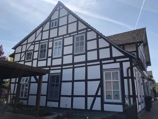 Gästezimmer Anna und Heini Fachwerkhaus mit weißen Wänden und dunklen Holzbalken, viele Fenster, ruhige Wohnlage, sonniger Tag.