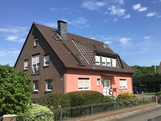 FeWo Süchting Ein zweigeschossiges rotes Backsteinhaus mit Garten steht unter einem strahlend blauen Himmel.