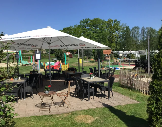 Gasthof und Hotel Rohrbach Sonnenterrasse mit Tischen, Stühlen und Sonnenschirmen im Grünen, umgeben von Bäumen und Spielplatz.