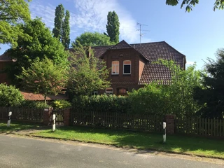 kloster-blick Ziegelgebäude mit Satteldach, umgeben von üppig grünen Bäumen und einem Holzzaun an einer ruhigen Straße.