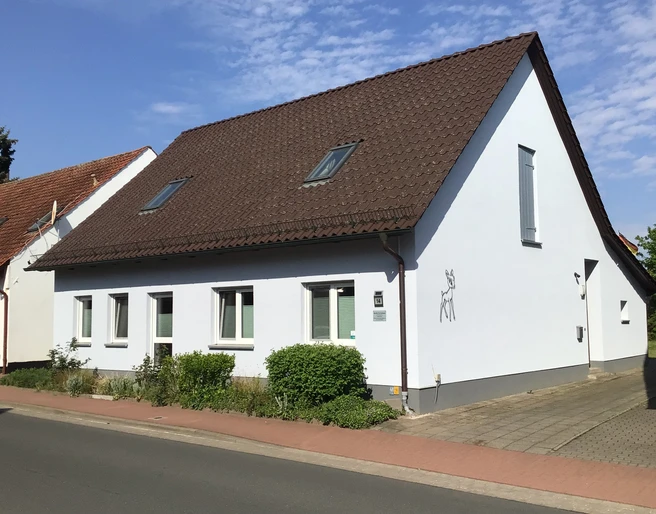 Burkis Ferienhaus Weiße Ferienhausfassade mit ziegelgedecktem Satteldach und einer aufgemalten Ziege an der Hauswand.