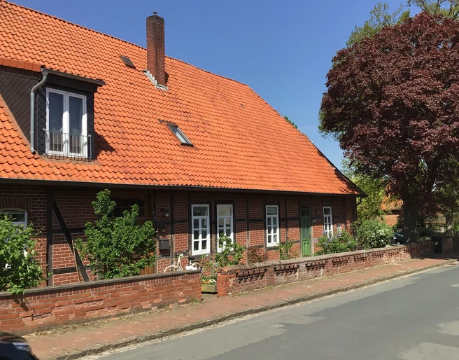 Ferienwohnung Runge Ein traditionelles rotes Ziegelhaus mit rotem Dach und Reet hinter einem gepflasterten Gehweg.