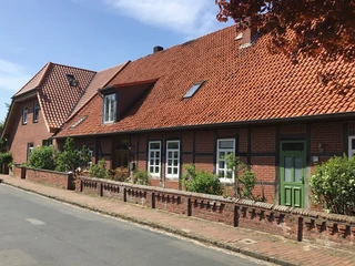 Ferienwohnung Runge Backsteinhaus mit roten Dachziegeln, grüner Tür und bunter Blumenrabatte entlang der Fassadenfront.