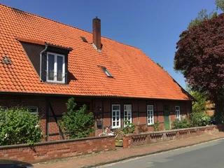 Ferienwohnung Runge Rotes Ziegelbauernhaus mit markantem Giebeldach und grünem Garten unter blauem Himmel.