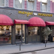 Mangal Restaurant Außenansicht mit rotem Vordach und eleganter Fassade in städtischer Umgebung.Exterior view with red canopy and elegant façade in an urban setting.