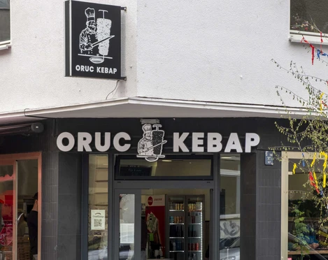 Oruc Kebap Die Außenansicht von Oruc Kebap zeigt den Eingang des Restaurants mit einem klaren, schwarzen Schild über der Tür und zwei Fahrrädern, die neben dem Eingang an der Wand lehnen.The exterior view of Oruc Kebap shows the restaurant entrance with a clear black sign above the door and two bicycles leaning against the wall next to the entrance.