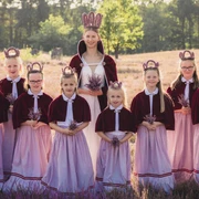 heidebluetenfest-amelinghausen-erlebniscard.jpg Eine Gruppe von Mädchen in traditionellen Dirndln und Kronen steht lächelnd in der blühenden Heide.