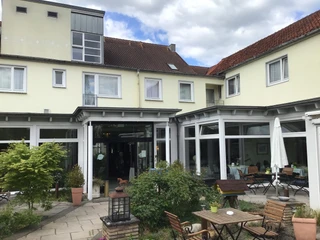 Hotel Höltje Hotel Höltje in Verden mit einladender Außenterrasse, Holzmöbeln und grüner Bepflanzung.