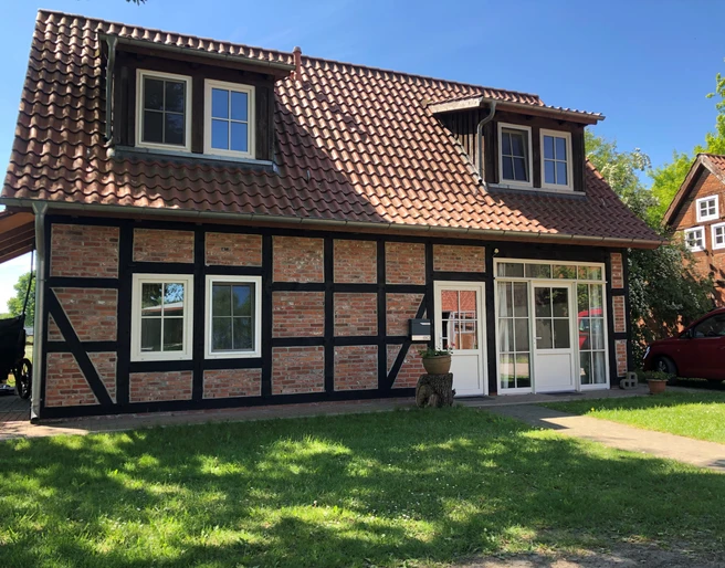 Fachwerkhaus Bruchhausen Fachwerkhaus mit roten Ziegeln und schwarzen Holzstreben, umgeben von grünem Rasen und blauen Himmel.