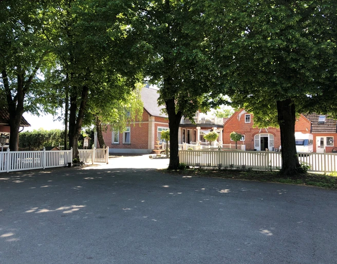 Reitstall zum Eichenhof Eingebettet in Bäume, zeigt sich ein Backsteinhaus eines Reitstalls mit weißem Zaun und Hof.