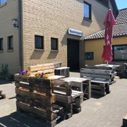 Außenbereich von Döhlings Gasthaus mit rustikalen Sitzmöbeln aus Paletten und einem Sonnenschirm.