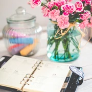 Bullet Journal Ein geöffneter Planer liegt auf einem Tisch neben einem Kerzenglas und einem Glas mit rosa Blumen.