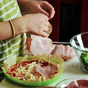 Kochen Das Bild zeigt eine Person, die eine Pizza belegt. Man sieht frischen Brokkoli und geschnittenen Aufschnitt auf dem Tisch.