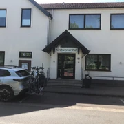 Eingangsbereich eines Hotels mit einem Schild "Kirchweyher Hof" über der Tür, Fahrradträger auf Auto.