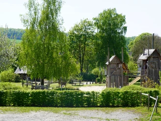 Ludowinengarten 1.JPG Ein Spielplatz aus Holz, umgeben von üppigen Bäumen und grünen Sträuchern, bietet Platz zum Entdecken.