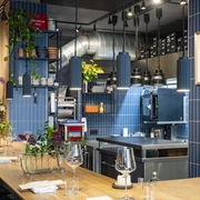 Pottkind Elegante, moderne Küche mit blau gekachelten Wänden im Restaurant; gedeckte Holztische mit frischen Blumen.Elegant, modern kitchen in the restaurant with blue-tiled walls; set wooden tables decorated with fresh flowers.