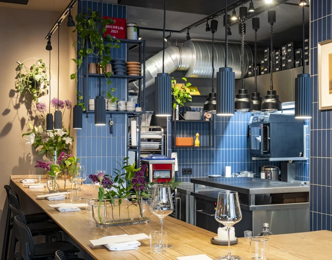 Pottkind Elegante, moderne Küche mit blau gekachelten Wänden im Restaurant; gedeckte Holztische mit frischen Blumen.Elegant, modern kitchen in the restaurant with blue-tiled walls; set wooden tables decorated with fresh flowers.