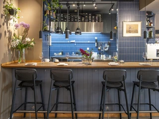 Pottkind Das Bild zeigt eine stilvolle, moderne offene Küche mit blauer Fliesenrückwand und einem Tresen mit Barhockern.The image shows a stylish, modern open kitchen with a blue tiled backsplash and a counter lined with bar stools.