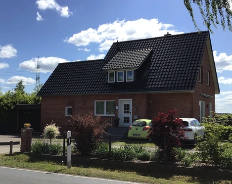 Gästehaus Meyer Backstein-Gästehaus Meyer vor blauem Himmel, mit Garten und zwei geparkten Autos im Vordergrund.