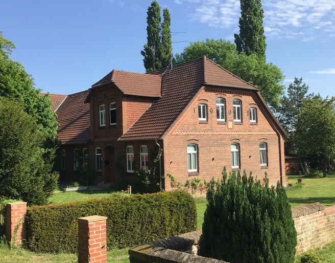 kloster-blick Ein rotes Backsteingebäude mit Satteldach steht vor einer Hecke, umgeben von grünen Bäumen und Rasen.