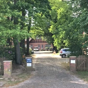 Ein einladender Hof mit Backsteingebäuden und umgebenden Bäumen, ein Auto parkt auf Kopfsteinpflaster.