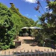 Ein grünes Landhaus mit üppigen Kletterpflanzen, Sonnenschirmen und einem Schotterweg im Garten.