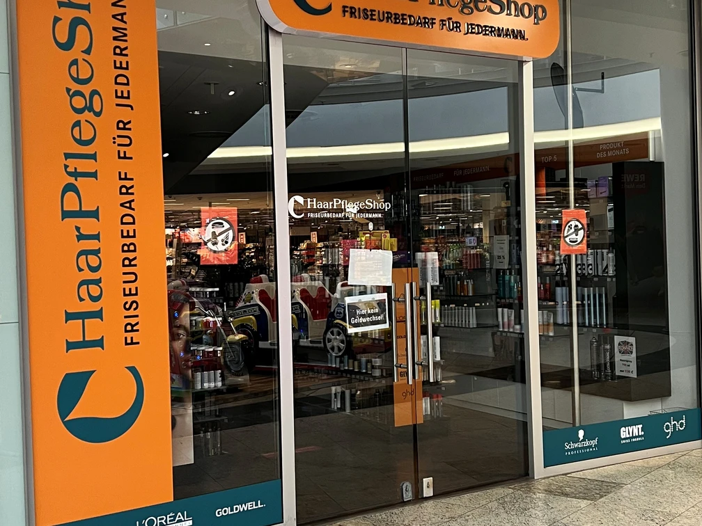 Haarpflegeshop.jpg Eingang eines Haarpflege-Shops mit Friseurbedarf und Markenlogos wie Wella, L'Oréal und Schwarzkopf.