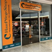 Haarpflegeshop.jpg Eingang eines Haarpflege-Shops mit Friseurbedarf und Markenlogos wie Wella, L'Oréal und Schwarzkopf.