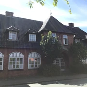 Historisches Backsteingebäude mit großen Sprossenfenstern und einem begrünten Eingangsbereich.