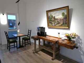 Frühstücks- und Aufenthaltsraum Heller Raum mit Kaffeemaschine, rustikaler Holzbank und zwei Stühlen an einem Tisch nahe einem Fenster.