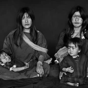 Amazonia Sebastiao Salgado Eine indigene Familie. Zwei Erwachsene sitzen zentral, während zwei Kinder auf ihnen ruhen. Die Gesichter sind mit traditionellen Mustern bemalt. Ein Ausdruck von Ruhe und Zusammenhalt dominiert die Szene.An indigenous family. Two adults sit in the center while two children rest on them. The faces are painted with traditional patterns. An expression of calm and cohesion dominates the scene.