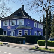 Café Clärchen in Velbert, Außenansicht Älteres, lila Gebäude mit weiß umrahmten Fenstern, umgeben von Bäumen und Hecken in Velbert.