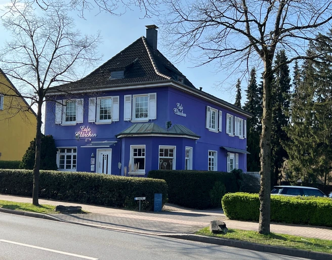 Café Clärchen in Velbert, Außenansicht Älteres, lila Gebäude mit weiß umrahmten Fenstern, umgeben von Bäumen und Hecken in Velbert.