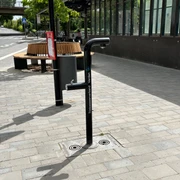 Trinkwasser-Brunnen_Bahnhof Trinkwasserbrunnen auf einem Bahnhofsplatz mit Sitzbank im Hintergrund, geeignet für durstige Reisende.