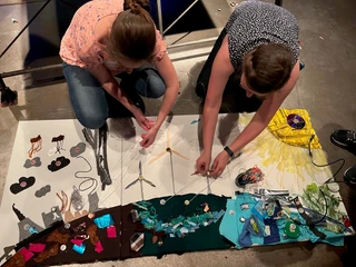 re:create Windmühlen Bild  Zwei Frauen gestalten ein kreatives Kunstwerk mit bunten Materialien am Boden liegend.Two women design a creative work of art with colorful materials lying on the floor.