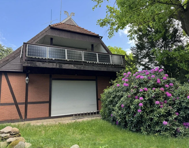 ferienwohnung-alscher-amelinghausen-solarbalkon-rhododendron.JPG Du siehst eine malerische, rustikale Unterkunft mit einem charmanten Reetdach. Davor blüht ein prächtiger Rhododendron.