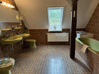 ferienwohnung-alscher-amelinghausen-retro-badezimmer.JPG Das Bild zeigt ein Badezimmer im Retro-Stil mit grünen Waschbecken und einem grünen WC. Rechts steht eine Badewanne. Oben ist ein Fenster, das Licht in den Raum lässt.