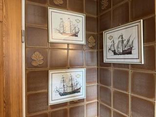 ferienwohnung-alscher-amelinghausen-retro-badezimmer-mit-Bilder.JPG Im Badezimmer der Ferienwohnung hängen drei gerahmte Bilder von historischen Segelschiffen an den Wänden mit braunen Fliesen. Die Fliesen haben ein Blumenmuster.