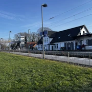 Bahnhof Augustfehn mit Fahrstuhl_2025 Bahnhof Augustfehn mit einem modernen Aufzug, Gleise, historische Gebäude und blauer Himmel im Hintergrund.