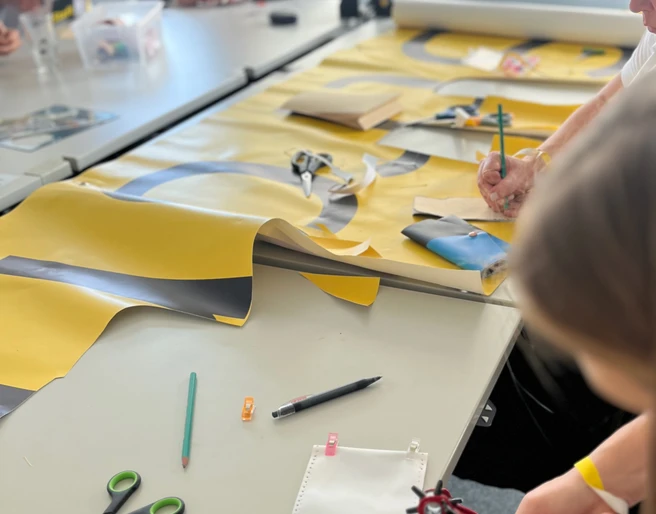 re:create Workshop <p>Menschen basteln an einem Tisch mit buntem Papier und Werkzeugen in einer hellen Umgebung.</p>