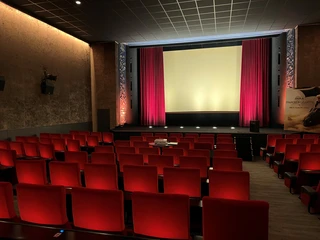 Filmhof Hoya Ein leerer Kinosaal mit roten Sitzen und einem beleuchteten Bildschirm, umrahmt von roten Vorhängen.
