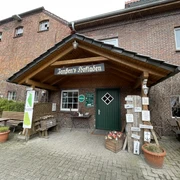 Außenansicht Hofladen Einladender Eingang zu 'Janßen's Hofladen' in einem Backsteingebäude, umgeben von Pflanzen und Schildern.