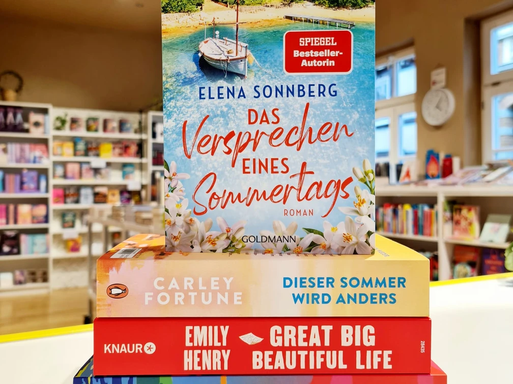 RomanceBC.jpg Ein Stapel bunter Bücher liegt vor dem Spiegel-Bestseller „Das Versprechen eines Sommertags“.