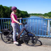 Schleusenkanal Balge Eine Radfahrerin steht auf einer blauen Brücke und blickt auf den Schleusenkanal Balge.